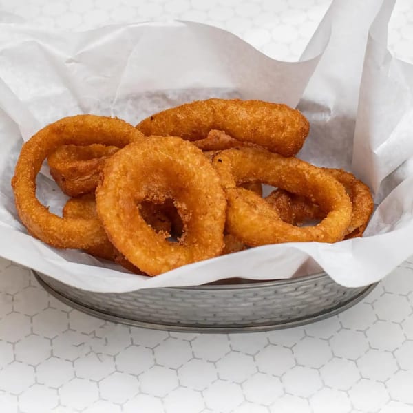 A basket of golden-brown, crispy onion rings from Sunshine Grill, served on white paper.