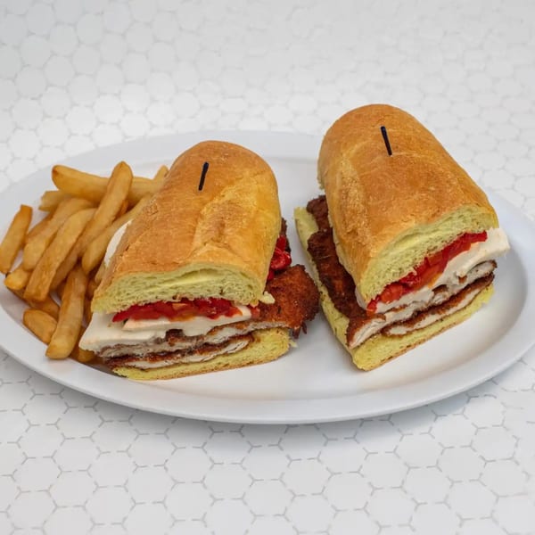 Two large chicken cutlet sandwiches with roasted red peppers and cheese, served with fries.
