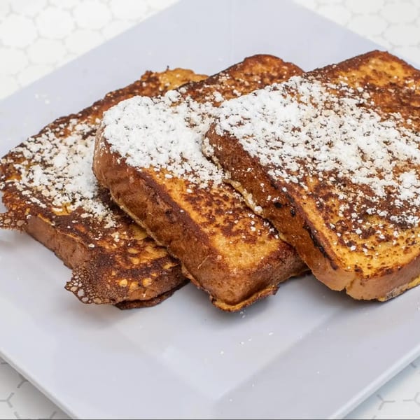 Three slices of golden-brown French toast, generously dusted with powdered sugar, on a white plate.