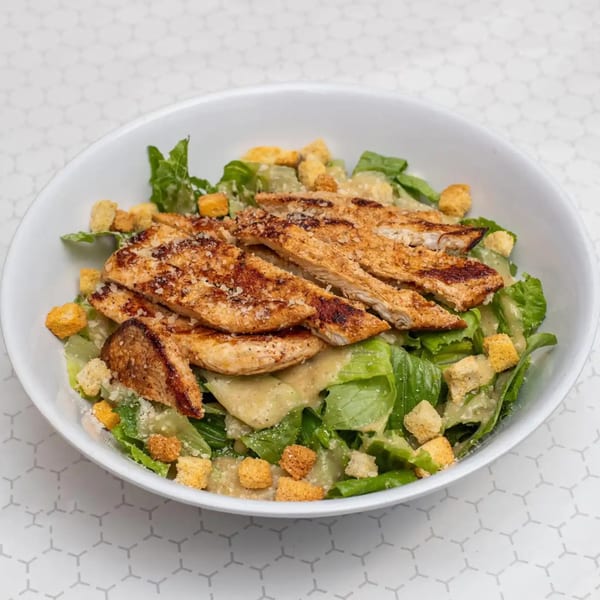 Grilled chicken Caesar salad with romaine lettuce, croutons, and dressing in a white bowl.