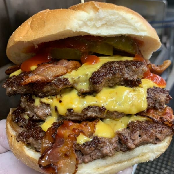 A triple-decker bacon cheeseburger from Sunshine Grill, topped with pickles and ketchup.