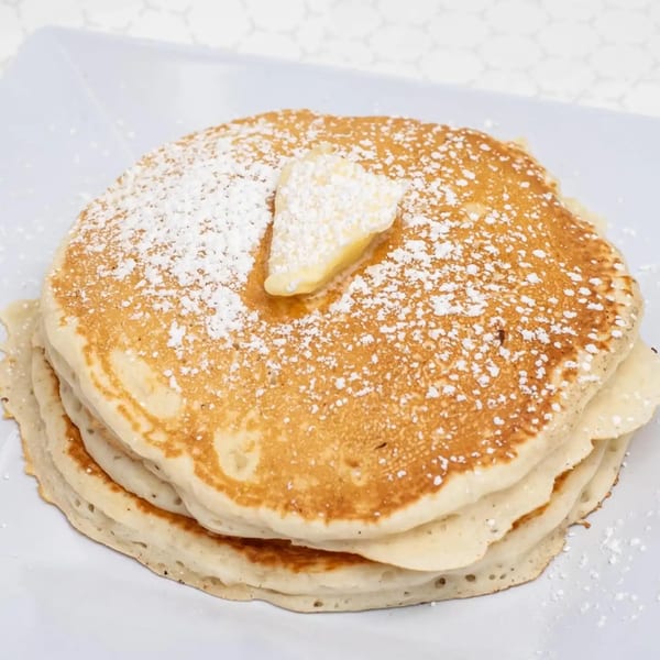 Stack of golden pancakes with powdered sugar and a pat of butter on a white plate.